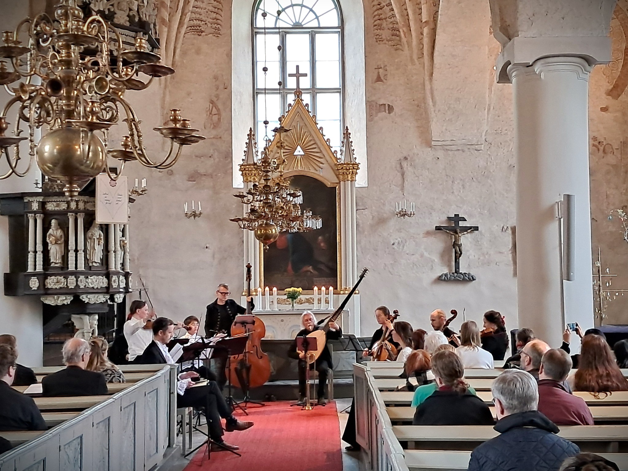 En orkester som spelar instrument i Sjundeå kyrka samt människor som sitter på kyrkans bänkrader och lyssna...