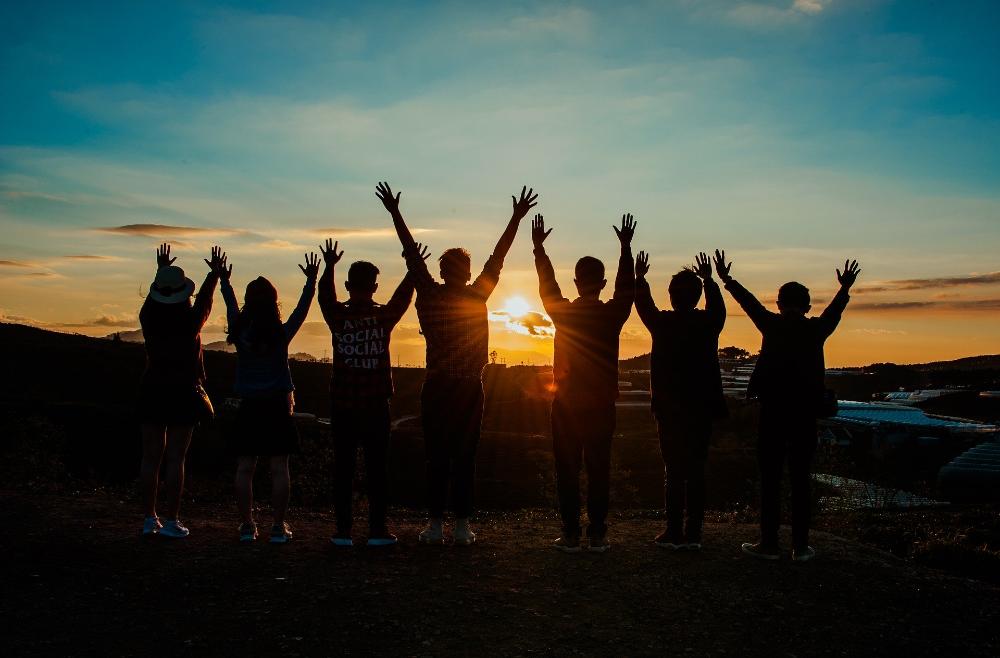 Ungdomar med händerna upp i luften framför en solnedgång
