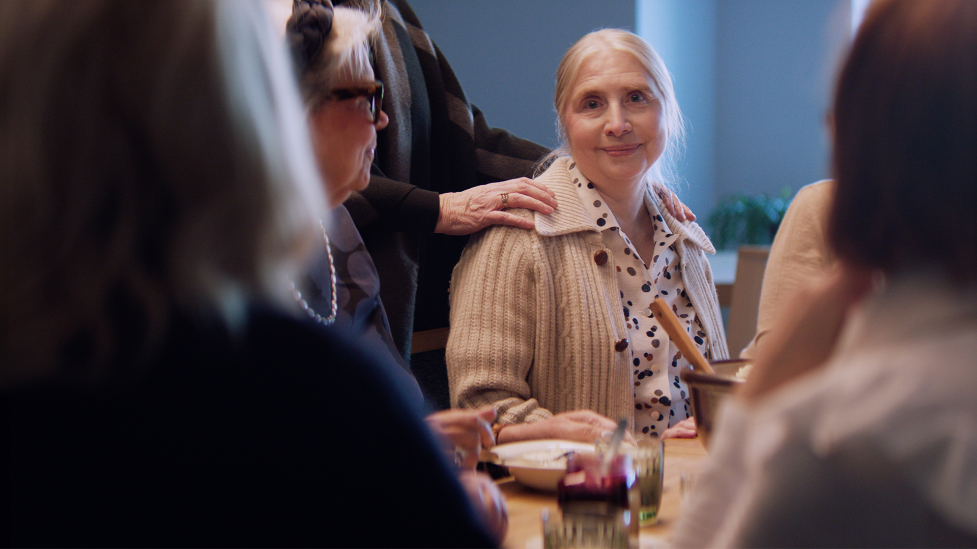 En senior omringad av människor ler mot kameran.